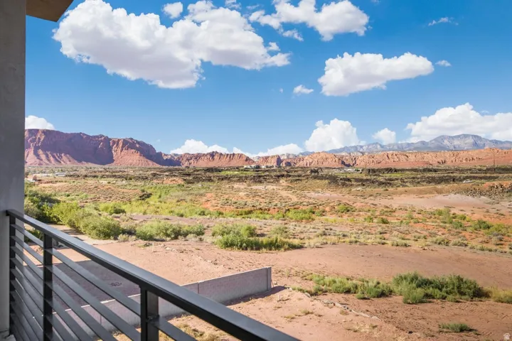 Balcony with a horizontal metal railing, featuring expansive desert scenery with distant red rock formations and mountains