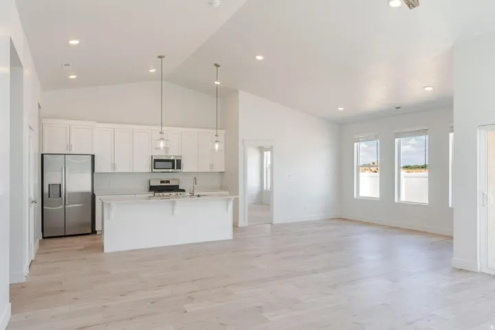 Vaulted ceilings, recessed lighting, wood-finish flooring, white cabinetry, and stainless steel appliances