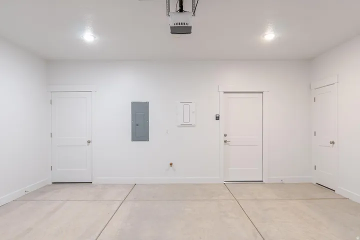 Concrete flooring, recessed ceiling lighting, three paneled doors, electrical panel, and white painted walls