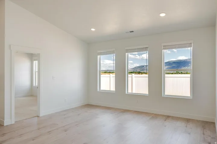 Spacious room featuring light wood-finish flooring, recessed ceiling lighting, a vaulted ceiling, and three windows with mountain scenery