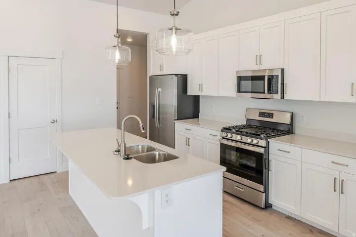 Kitchen featuring white cabinetry, stainless steel appliances, a center island with a double basin sink, and wood-finish flooring