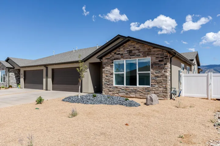 Stone facade detailing, stucco exterior finish, attached two-car garage, white vinyl fencing, and gravel landscaping