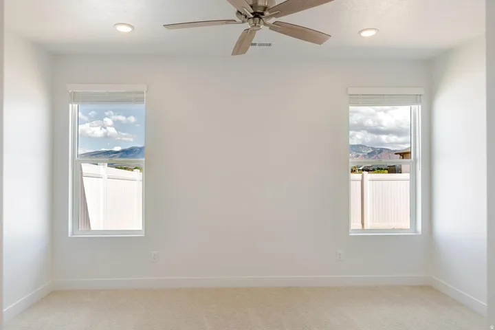 Recessed lighting, ceiling fan, two windows with blinds, and light-colored carpeting