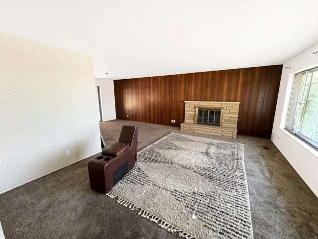 Interior featuring a stone-clad fireplace, wood paneling, and a large window
