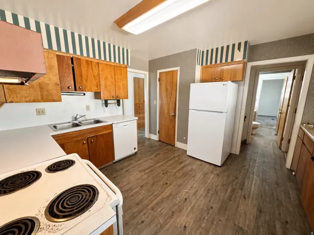 Kitchen featuring wood-finish flooring, wood cabinetry, white countertops, and white appliances