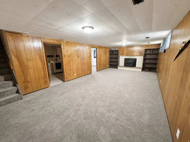 Spacious room with wood-paneled walls, built-in shelving, fireplace, light-colored carpeting, and a drop ceiling with recessed lighting