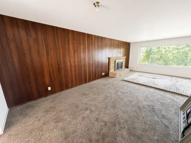 Wood panel accent wall, brick fireplace, expansive window, and carpeting