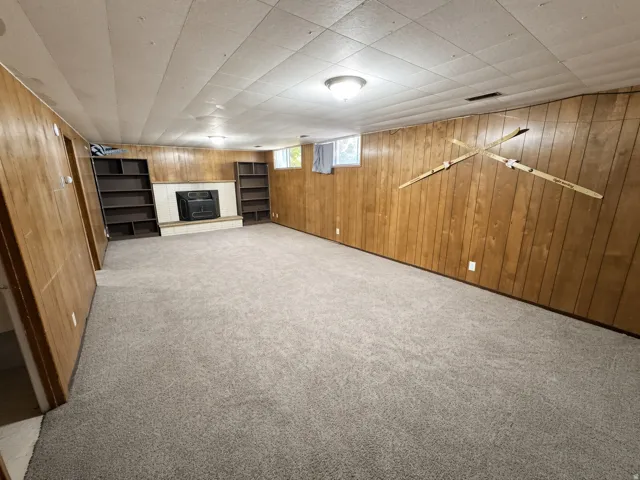 Spacious room with wood paneling, carpet flooring, a central fireplace with a tile surround, and built-in shelving