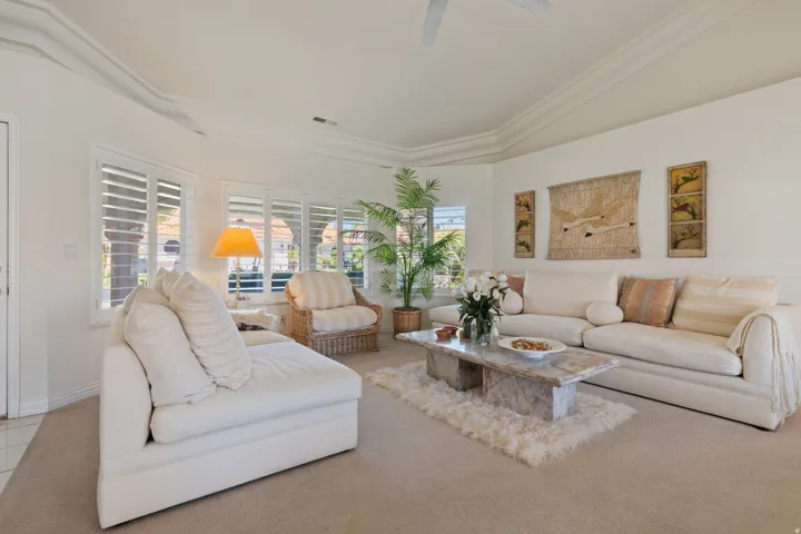 Recessed ceiling with decorative molding, ceiling fan, multiple windows with plantation shutters, and a stone-finish coffee table