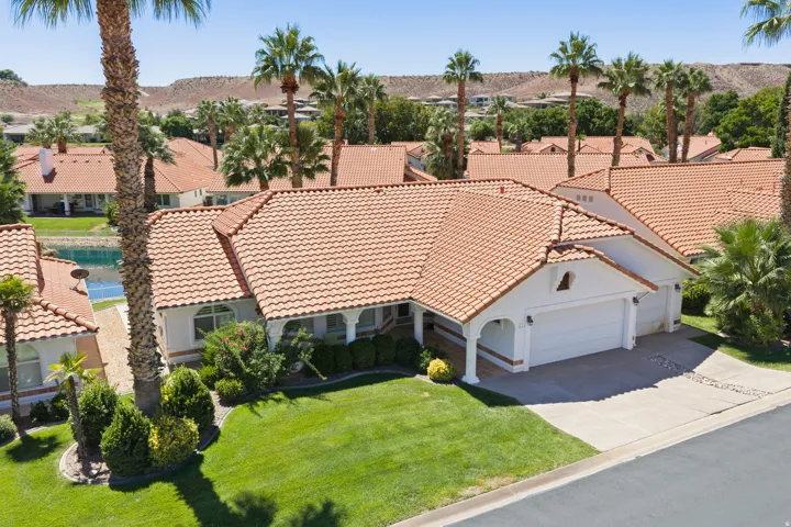 Terracotta-style roof, mature palm trees, manicured lawn, attached garage, and paved driveway