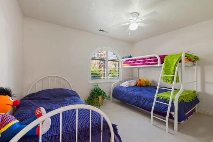 Arched window with plantation shutters, ceiling fan with light fixture, and neutral wall color