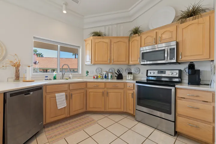 Kitchen featuring light wood cabinetry, stainless steel appliances, white countertops, and a white tile backsplash