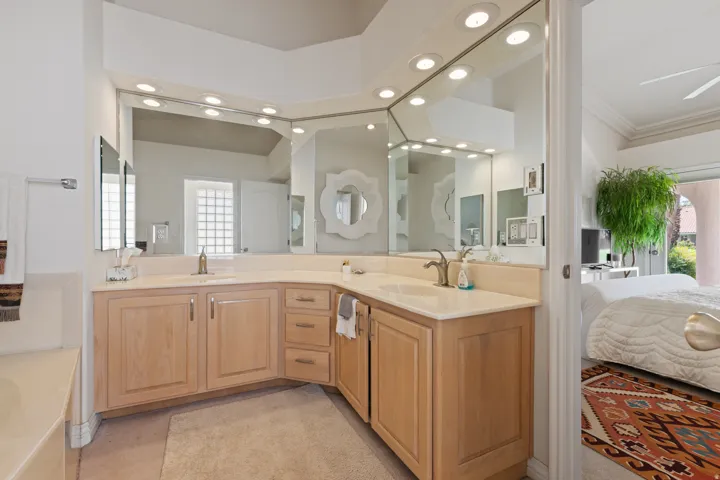 Corner vanity with dual sinks, light wood-finish cabinetry, and expansive wall-mounted mirrors