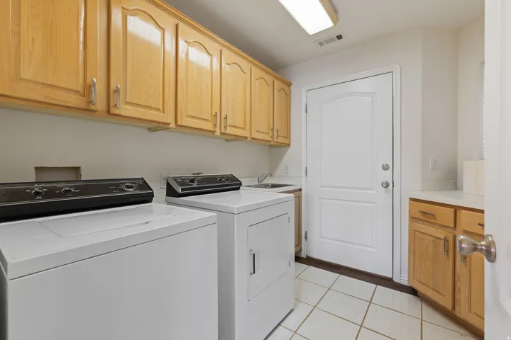 Utility room featuring abundant cabinetry, a built-in sink, and tile flooring
