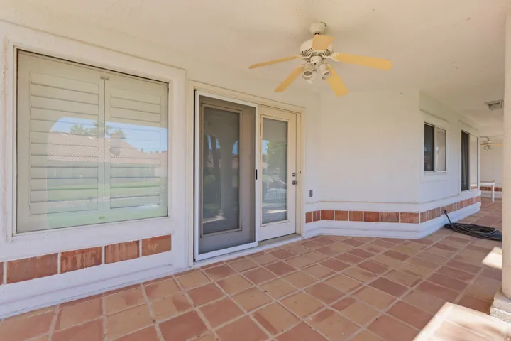 Covered patio with terracotta tile flooring, white stucco walls, decorative tile wainscoting, and a ceiling fan with integrated lighting