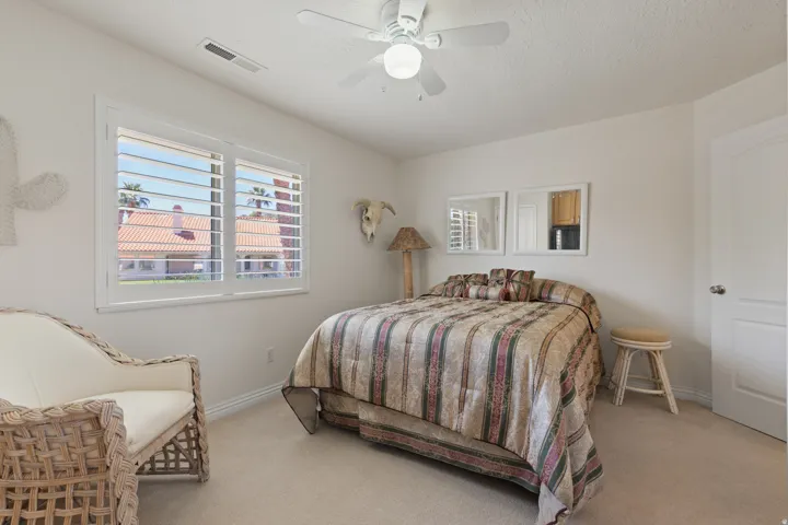 White interior walls, window with white plantation shutters, ceiling fan with integrated lighting, paneled interior door, and neutral-toned carpeting