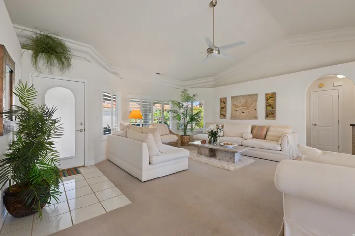 Vaulted ceiling with crown molding, ceiling fan, arched entryways, and plantation shutters