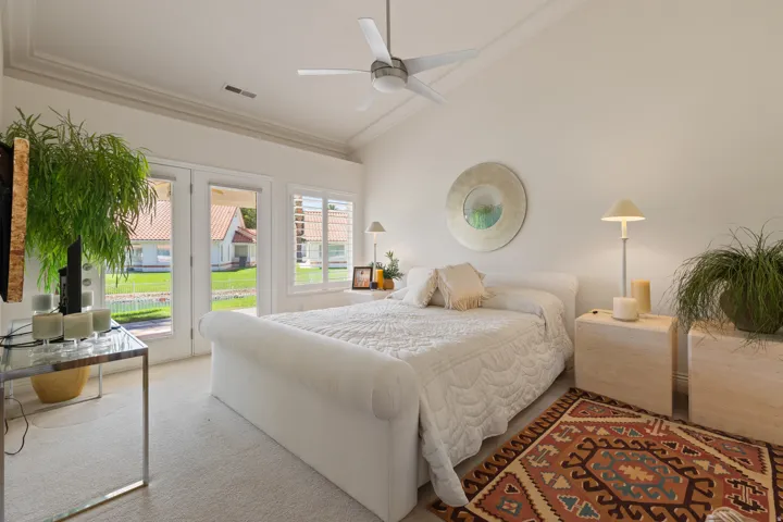 Vaulted ceiling with a ceiling fan, crown molding, double French doors, and an additional window with plantation shutters
