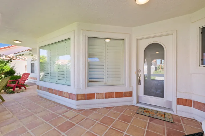 Covered entry with terra cotta tile flooring, arched entry door, and large bay windows with plantation shutters