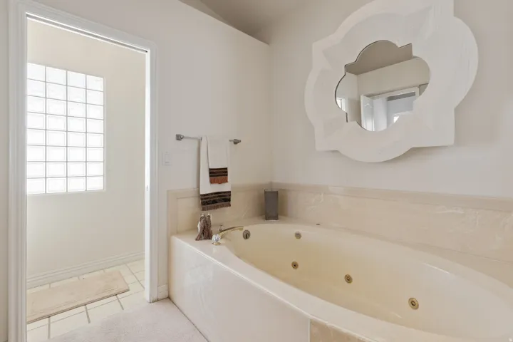 Jetted soaking tub with a tiled surround, wall-mounted towel bar, and glass block window