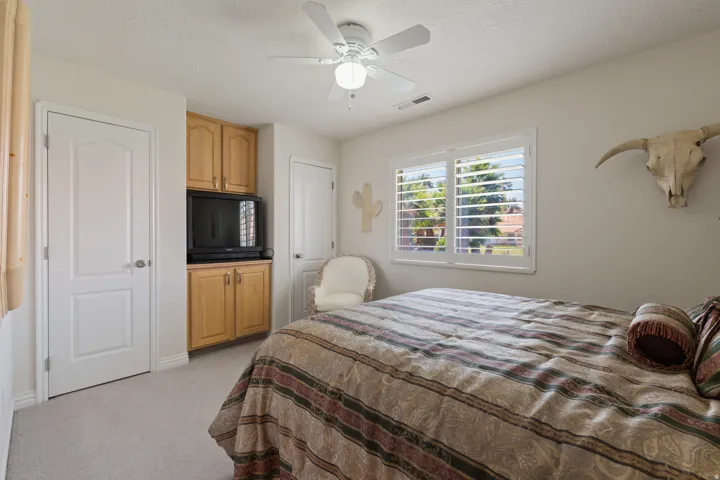 Built-in cabinetry, window with plantation shutters, ceiling fan with integrated lighting, light-toned carpeting, and panel doors