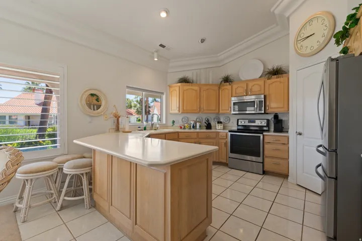 Kitchen featuring a large island with countertop seating, light wood cabinetry, stainless steel appliances, and tiled flooring