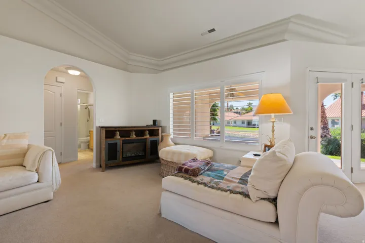 Tray ceiling with crown molding, arched entry, plantation shutters, and glass-paneled French doors