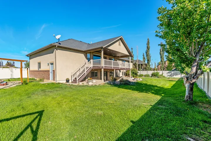 Expansive green lawn, multi-level deck with white railing, and a covered patio area