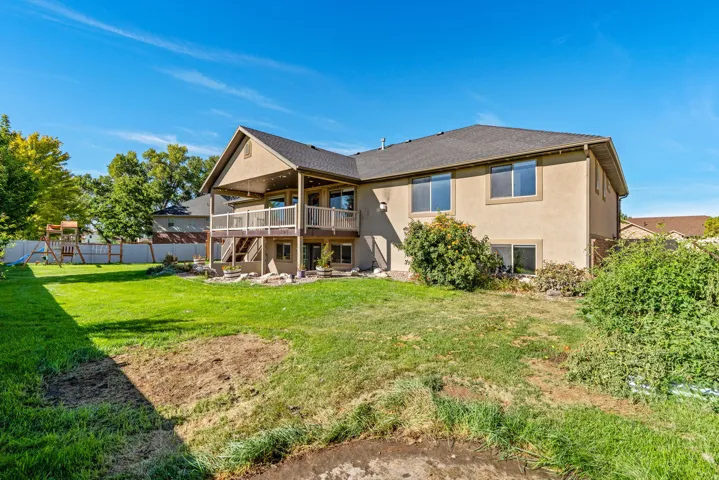 Expansive backyard featuring a manicured lawn, a two-story exterior with an upper-level covered deck, and a lower-level patio