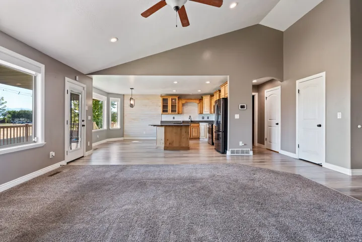 Vaulted ceiling with recessed lighting and a ceiling fan, light wood-finish flooring, and a kitchen featuring wood cabinetry and black appliances
