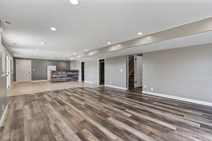 Spacious open-concept room featuring wood-finish flooring, recessed lighting, and a built-in bar with stone-look countertop