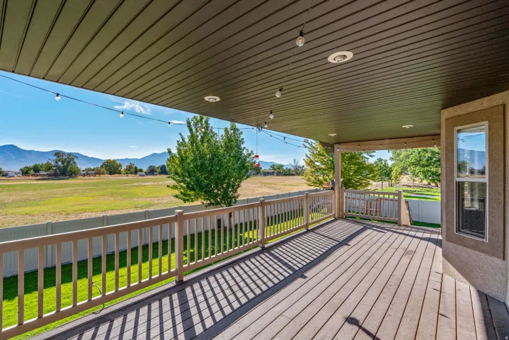 Expansive covered deck featuring wood-finish flooring, white railing, and recessed lighting