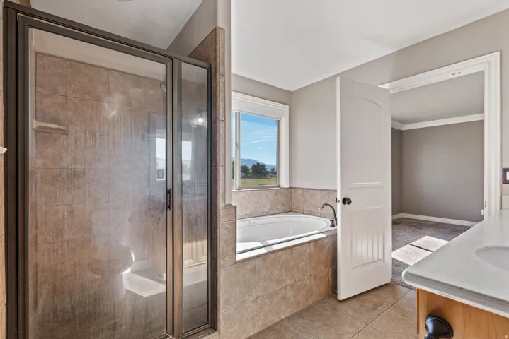 Tiled walk-in shower with a glass enclosure, jetted soaking tub with tiled surround, and a vanity featuring an integrated sink with a light-colored countertop