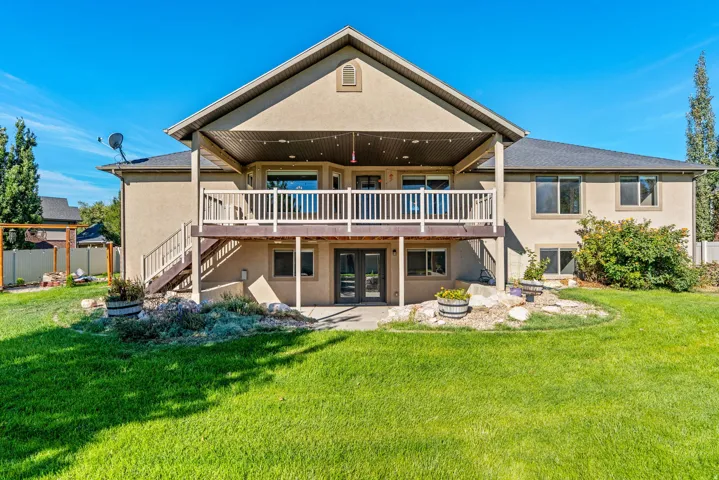 Expansive rear exterior featuring a two-story design, covered upper-level deck, lower-level patio, and a manicured lawn