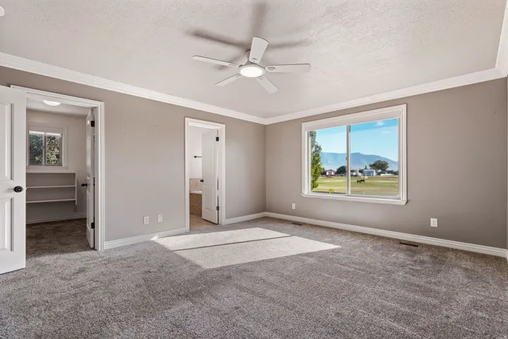 Expansive carpeted room featuring a ceiling fan, crown molding, and a large window with a mountain backdrop