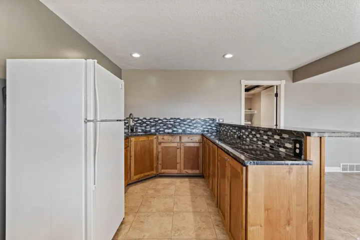 U-shaped counter with wood cabinetry, black countertops, and a tiled backsplash