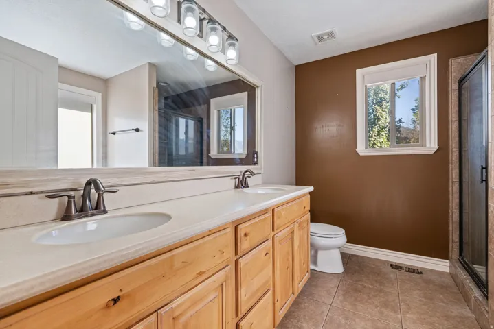 Dual vanity with integrated sinks, wood-finish cabinetry, bronze-finish fixtures, and a glass-enclosed shower