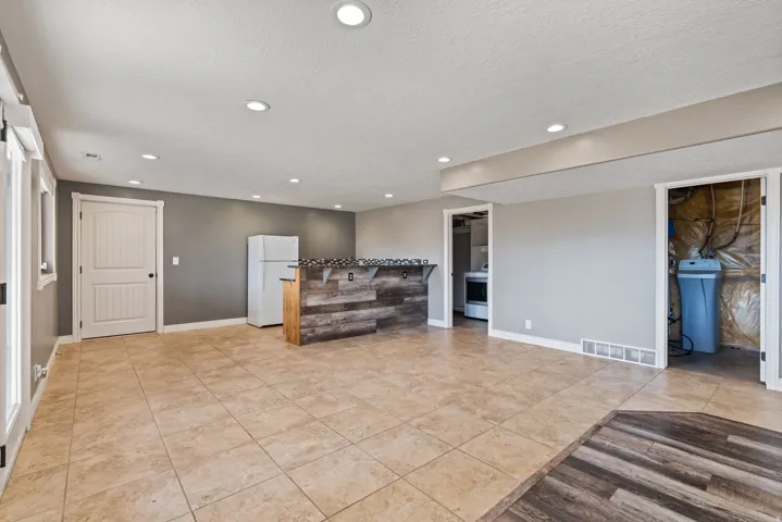 Spacious room featuring neutral tile flooring, recessed lighting, and a built-in bar with a wood-finish facade and stone-look countertop
