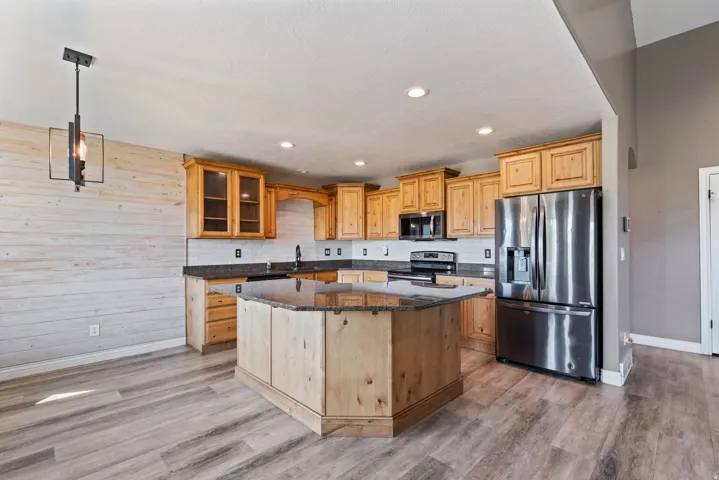 Kitchen featuring wood-finish flooring, wood cabinetry, stainless steel appliances, a center island with a stone countertop, and a tile backsplash
