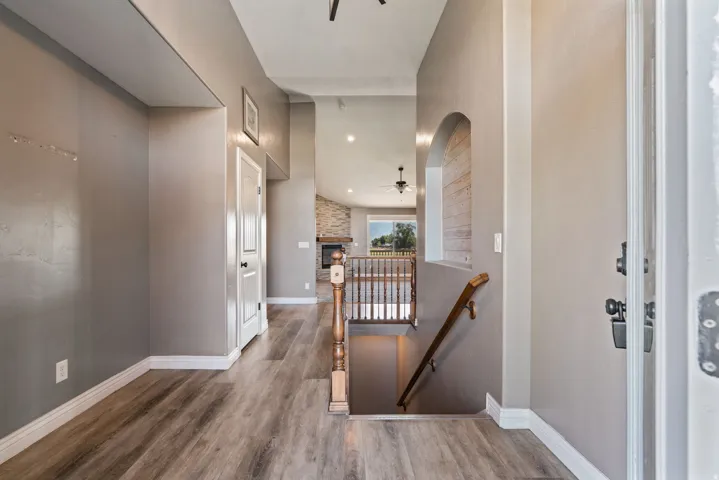 Wood-finish flooring, staircase with wood railing, recessed lighting, arched wall niche, and vaulted ceiling