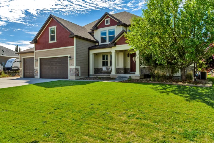 Two-story residence featuring a covered front porch, stone and siding exterior, two-car garage, and mature landscaping