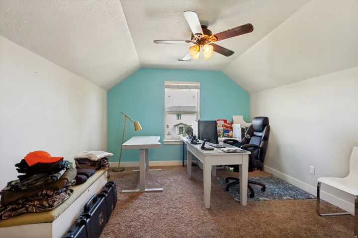 Carpeted room with a vaulted ceiling, a ceiling fan with integrated lighting, and a single window