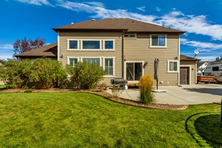 Expansive backyard with a manicured lawn, concrete patio, and mature shrubbery