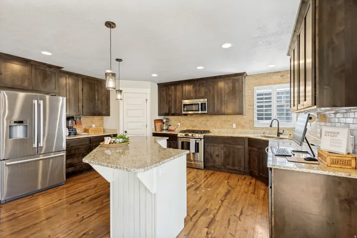 Wood-finish flooring with dark wood cabinetry, stainless steel appliances, and a central island with a light-toned countertop