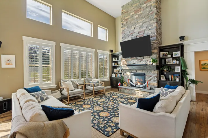Vaulted ceiling with transom windows, floor-to-ceiling stone fireplace, built-in shelving, and wood-finish flooring