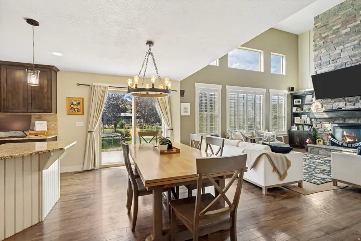 Open-concept living space featuring wood-finish flooring, a stone-clad fireplace, and a vaulted ceiling