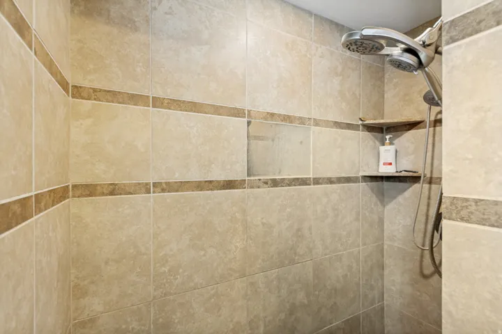 Tiled shower enclosure featuring light-toned large format tiles, decorative horizontal accent bands, and a built-in corner shelf