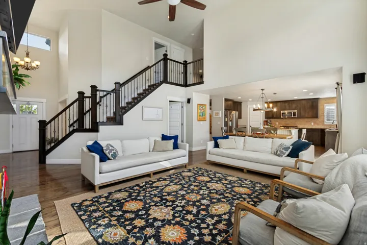 Vaulted ceilings with a ceiling fan, wood-finish flooring, staircase with dark wood newel posts and balusters, open concept kitchen, and upper transom windows