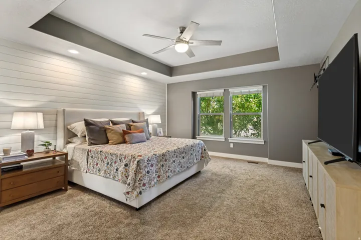 Tray ceiling with recessed lighting, ceiling fan, shiplap accent wall, and dual windows