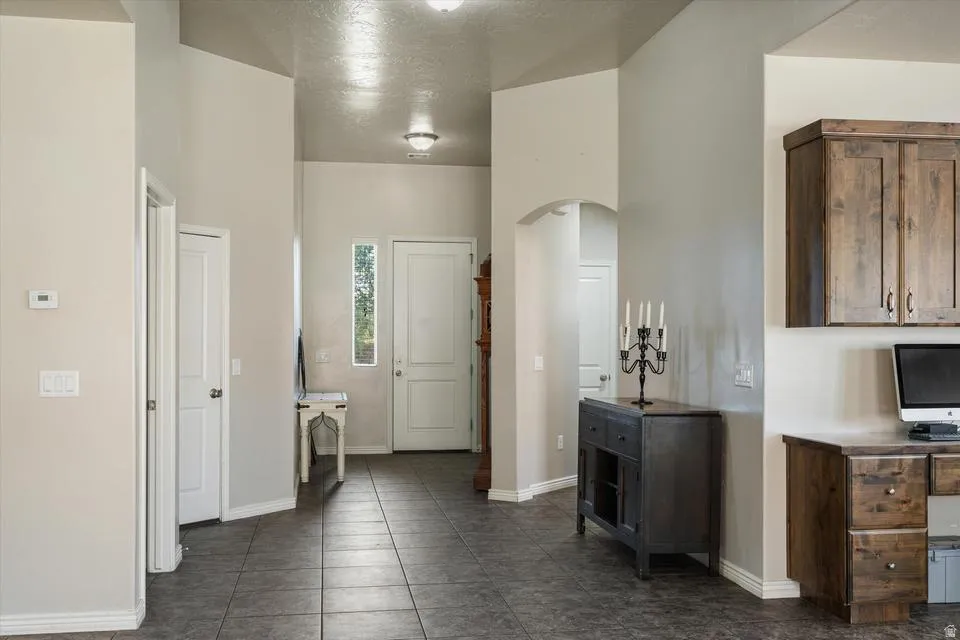 Entryway featuring tile flooring, a built-in wood-finish desk, wood-finish cabinetry, and an arched doorway